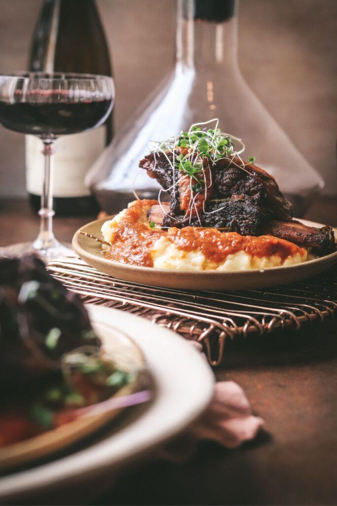 Two plates of Champagne-braised short ribs served over mashed potatoes, garnished with fresh parsley and a glass of Champagne