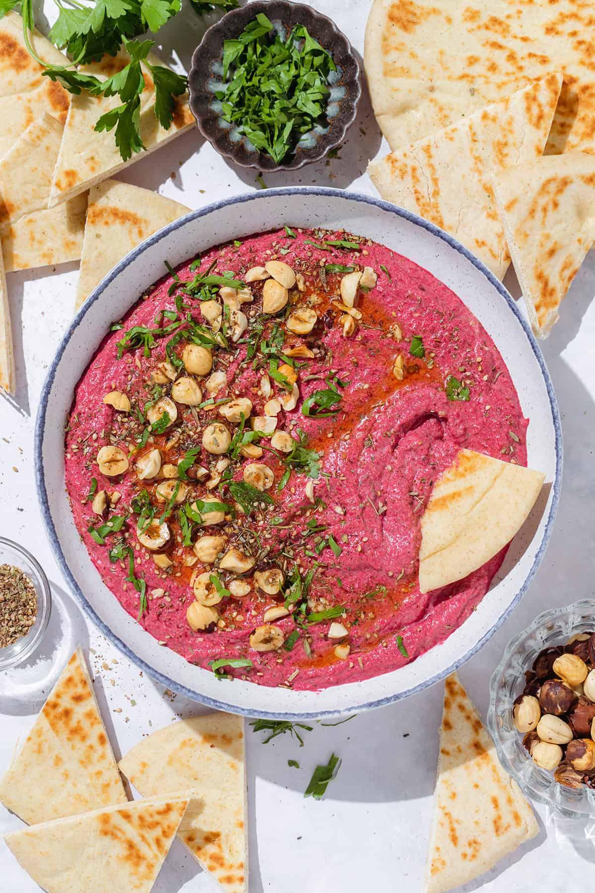 A bowl of roasted beet and goat cheese dip served with pita chips and crudités