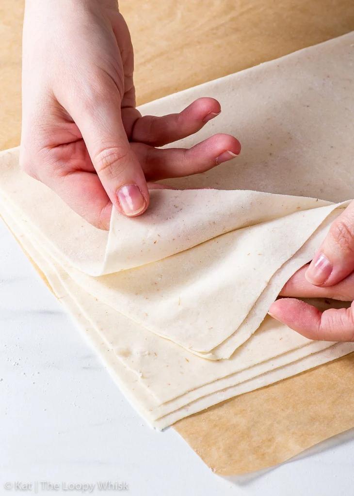 Close-up shot of hands carefully layering phyllo dough, showing the detail and care involved.
