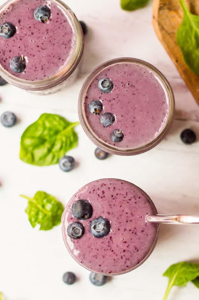 a person adding a handful of fresh spinach to a blender already containing berries and almond milk