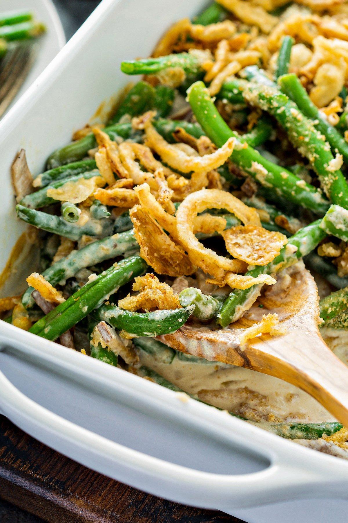 Hands scooping crispy onion green bean bake from a large baking dish