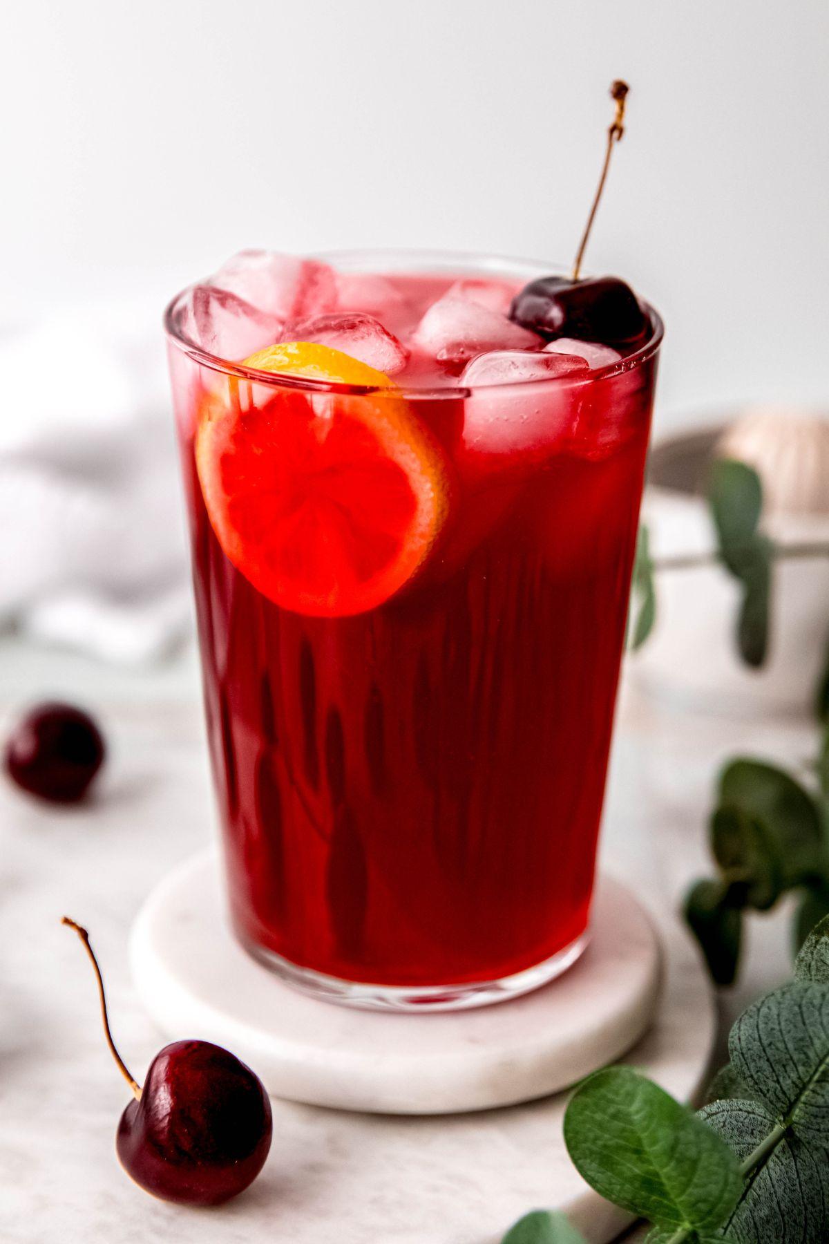 cherry almond lemonade in a clear glass with ice cubes and garnishes
