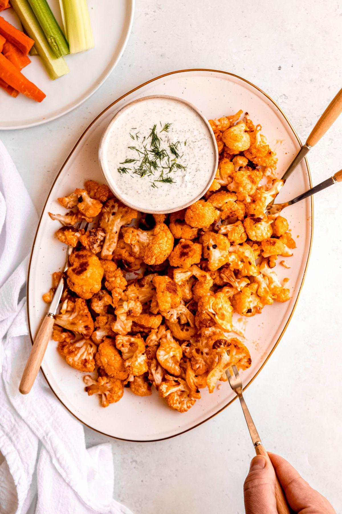 Hand reaching for a crispy cauliflower bite from a festive platter.