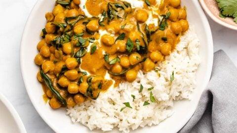 A richly colored bowl of chickpea and spinach curry with basmati rice and fresh cilantro, steam rising, in a rustic setting.