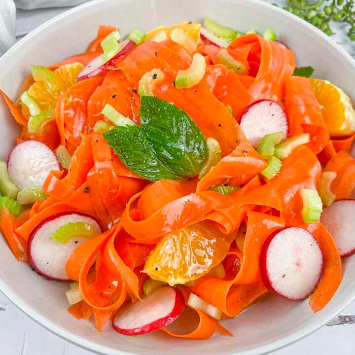 overhead shot of a colorful carrot and orange salad in a white ceramic bowl