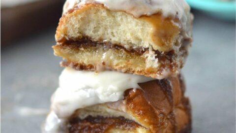 Thick cream cheese icing being generously drizzled over a cooling cinnamon roll loaf, filling all crevices