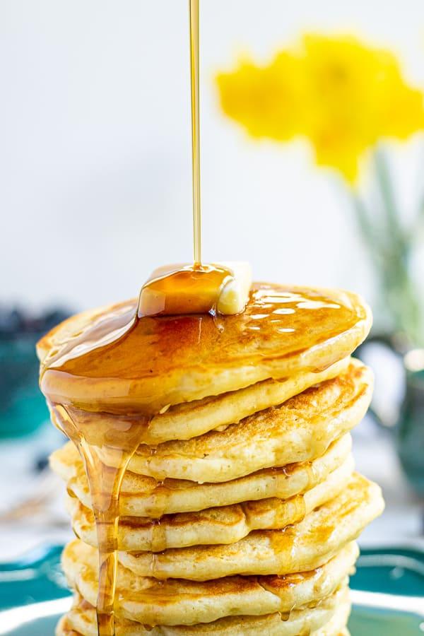 close-up of cooked pancakes with maple syrup being poured over