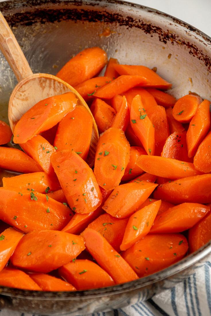 Close-up of golden honey glazed carrots steaming in a non-stick skillet on a stovetop