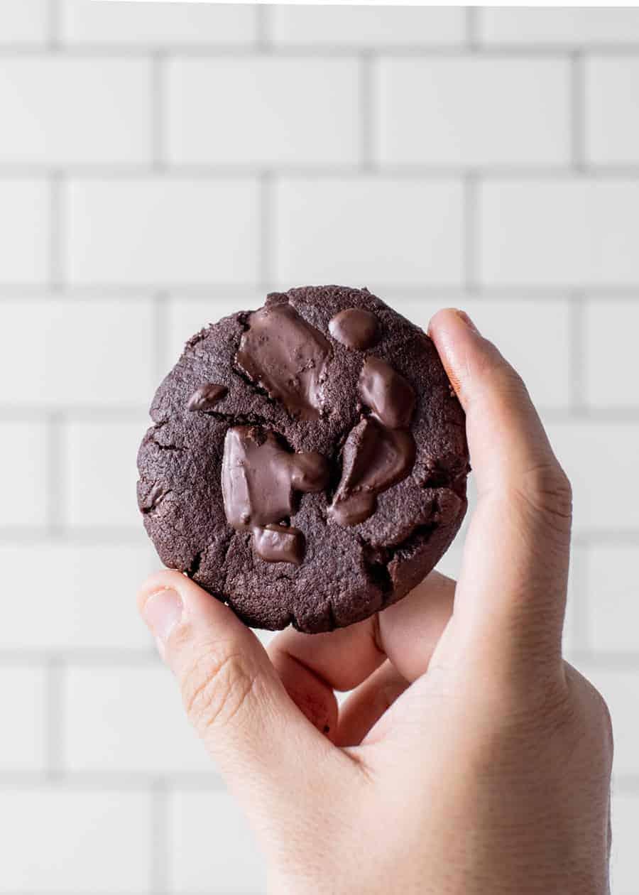 Hand holding a perfectly baked rich cocoa sugar cookie, slightly broken to show the fudgy interior.