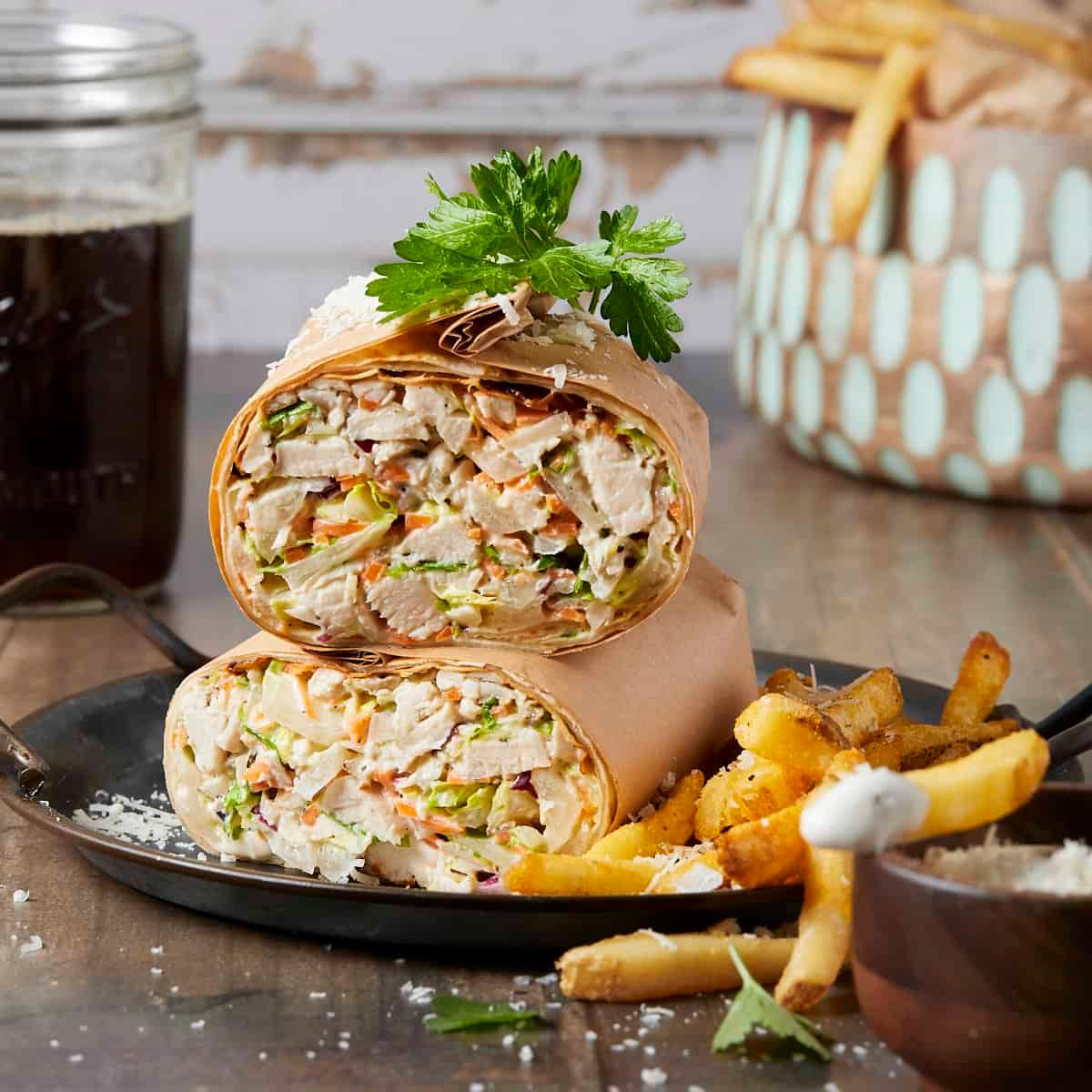 Close-up of a Chicken Caesar Wrap cut in half, revealing the filling, next to a pile of Parmesan crisps
