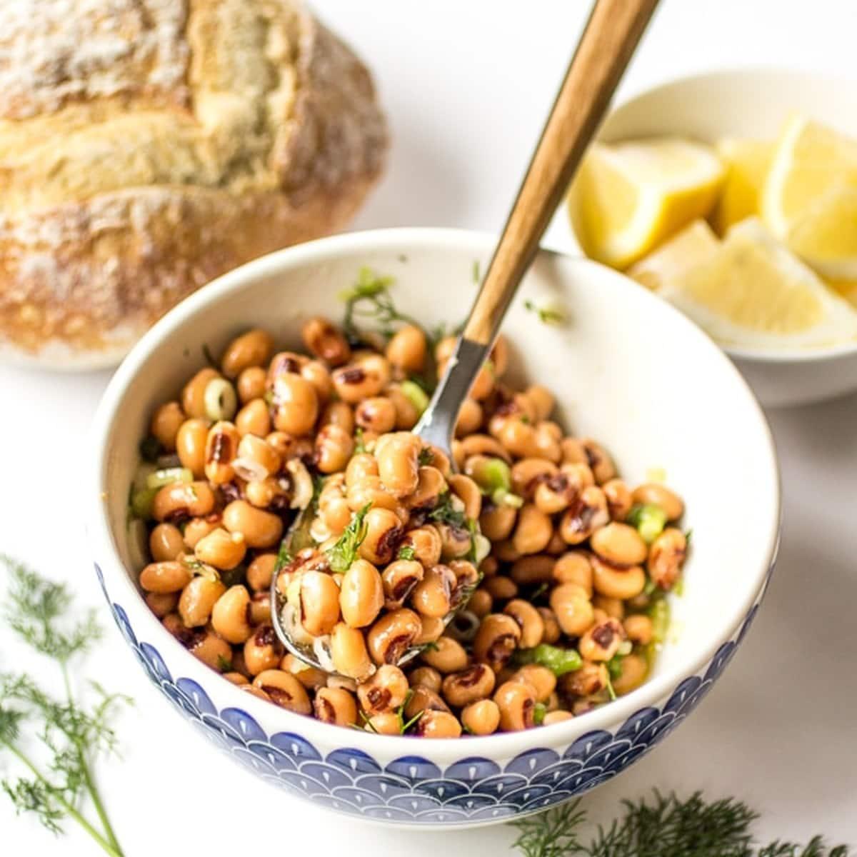 a person drizzling lemon-herb vinaigrette over a barley and black-eyed pea salad