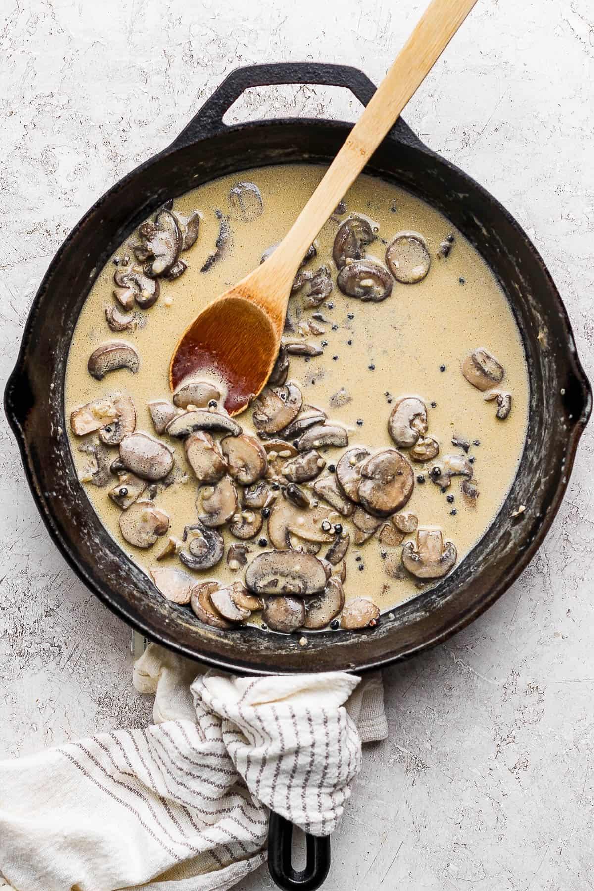 Homemade creamy mushroom sauce simmering in a skillet with fresh herbs