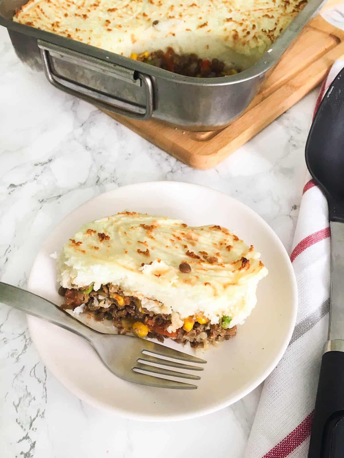 Close-up shot of a slice of Lentil Shepherd's Pie being lifted from the baking dish, showing the layers