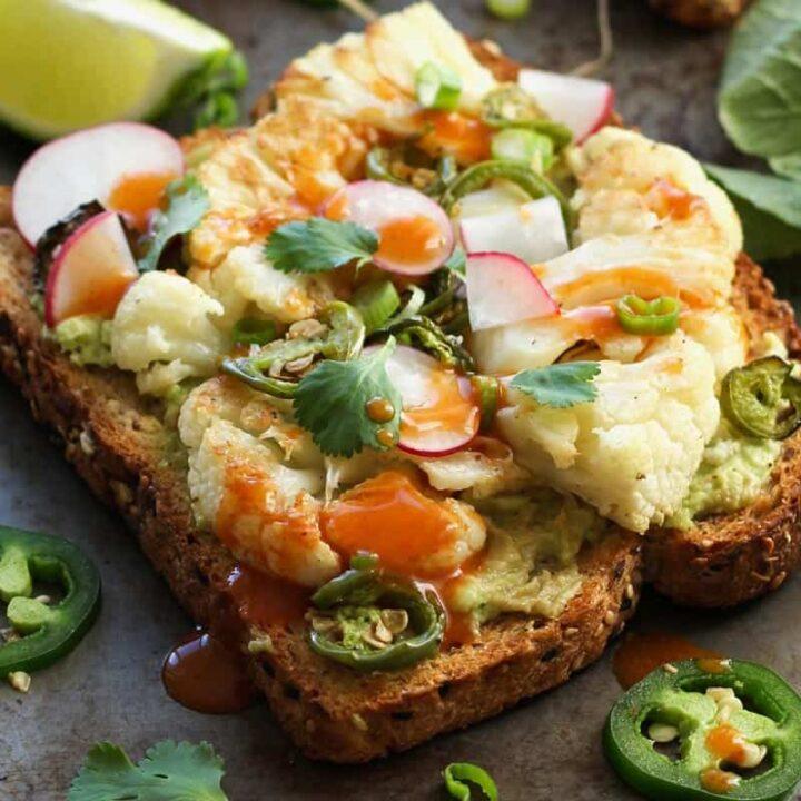 Close-up shot of a hand drizzling hot sauce on avocado toast