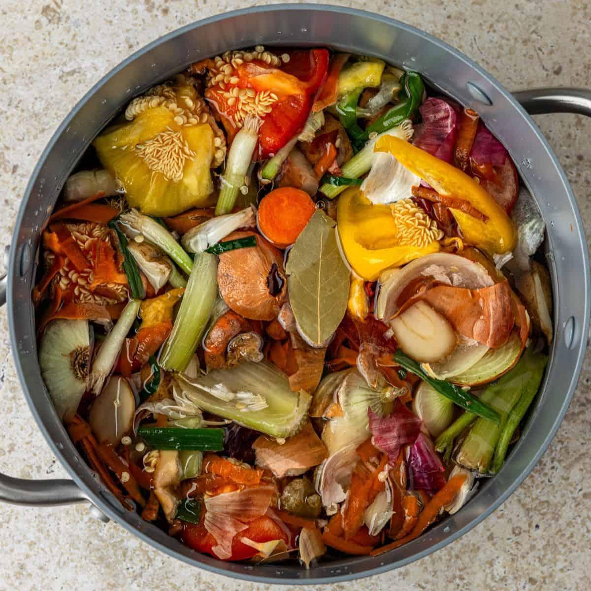 A rustic wooden table with a simmering pot of vegetable broth, various vegetable scraps around it