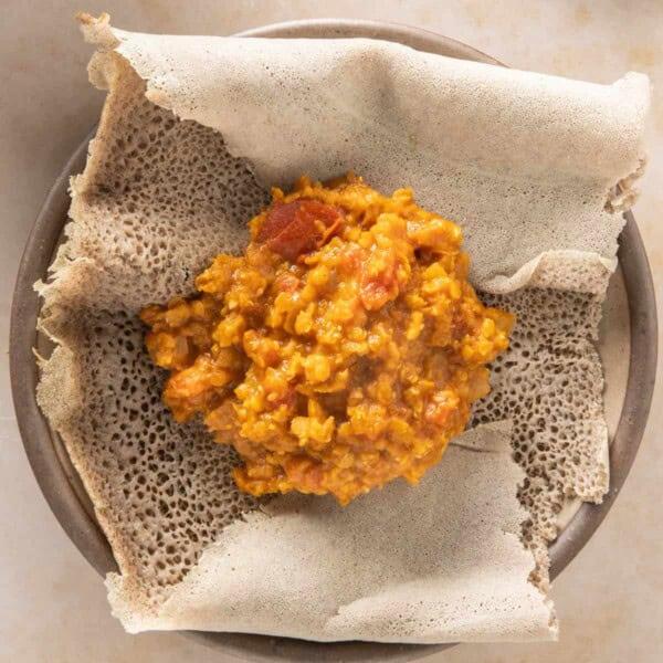 A steaming plate of injera topped with a generous serving of shiro wat, garnished with fresh herbs.