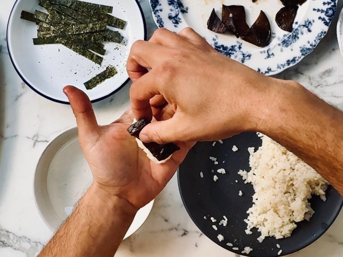 Close-up of someone preparing Eel Mango Sticky Rice Sushi rolls