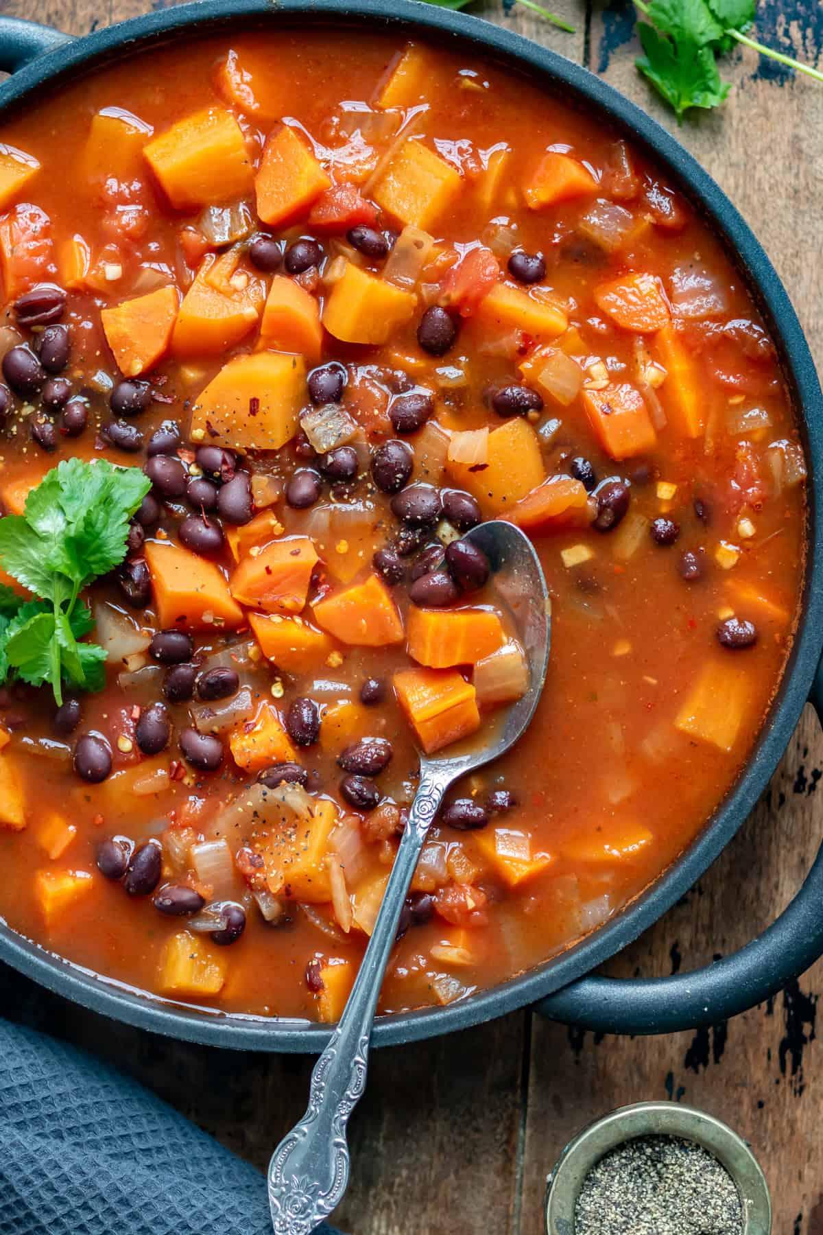 Close-up shot of a steaming bowl of sweet potato and black bean soup garnished with fresh cilantro and a dollop of sour cream