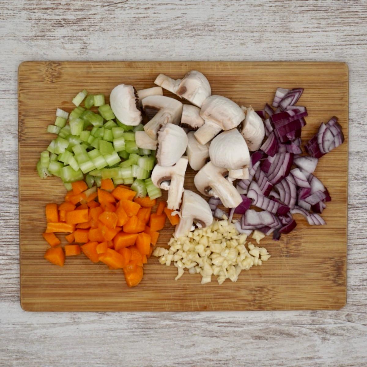 Assortment of fresh chopped vegetables (carrots, celery, onion, garlic) for lentil stew on a wooden cutting board