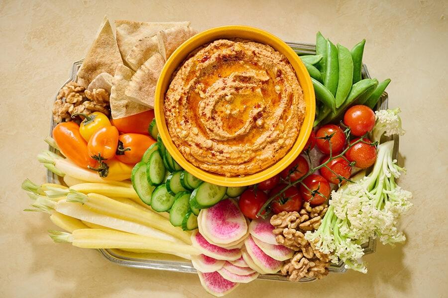 a vibrant close-up shot of the ingredients for roasted red pepper and walnut hummus, including red bell peppers, walnuts, chickpeas, garlic, lemon, and olive oil