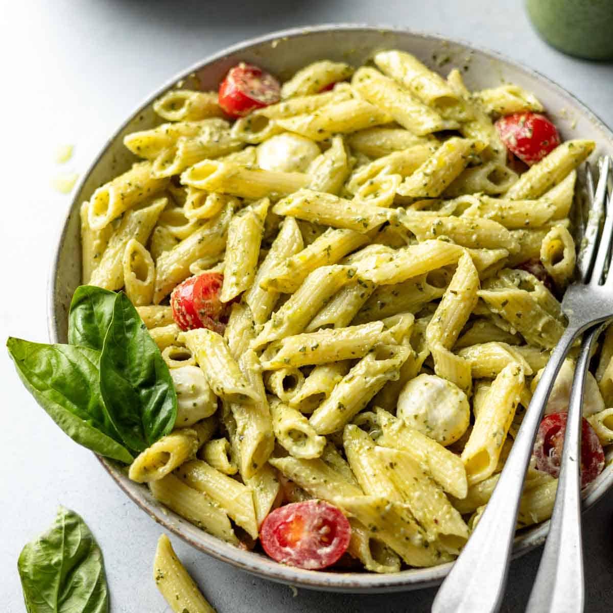 Close-up shot of a plate of gluten-free pasta with creamy pesto sauce and tender chicken, garnished with fresh basil leaves