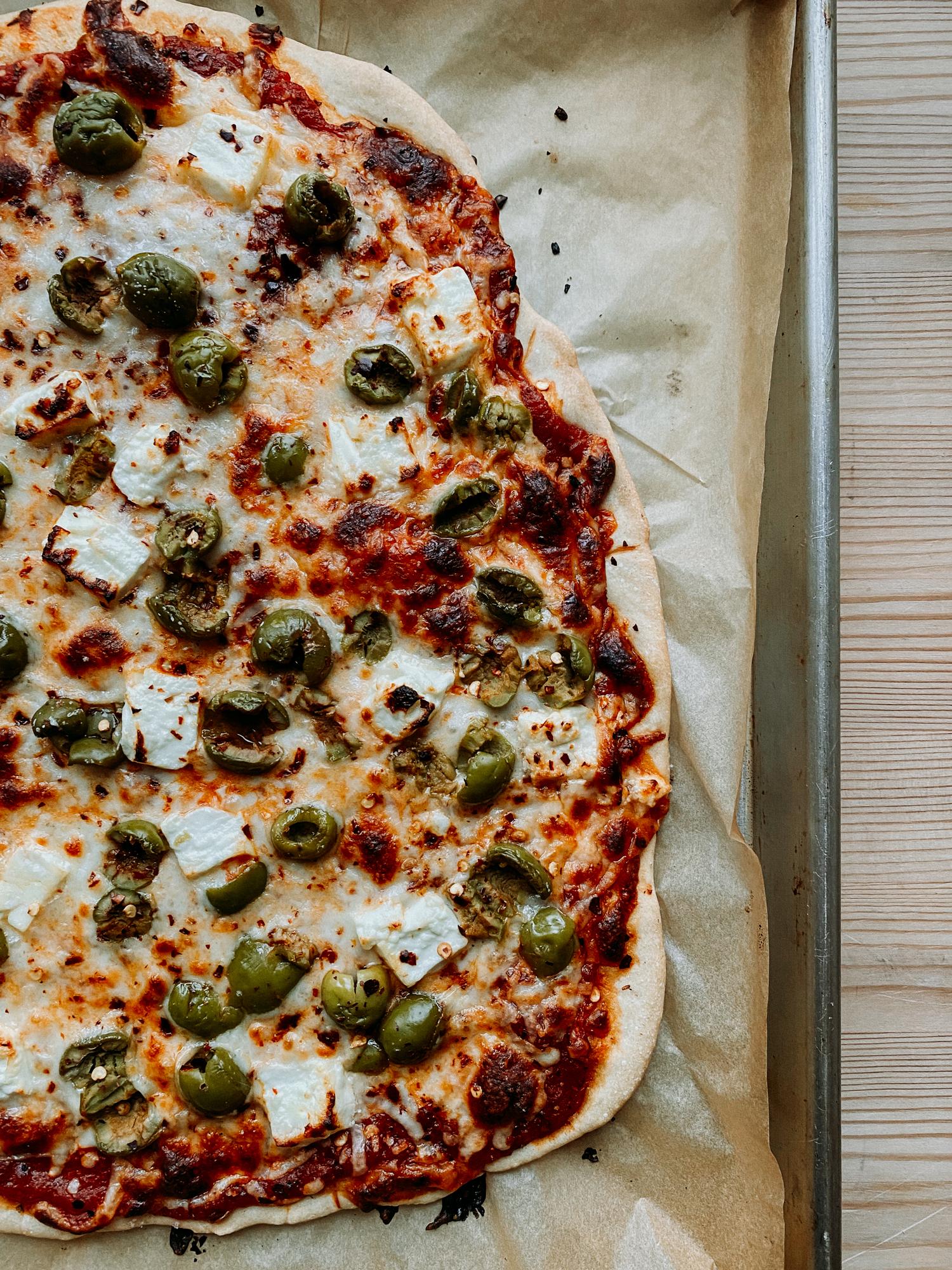 A rustic, delicious pizza with green olives, feta cheese, and a sprinkle of oregano