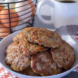 Hands preparing pancake batter in a bowl, with small sausage patties cooking in the background