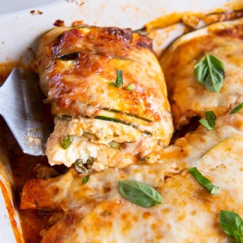 Close-up of a slice of zucchini lasagna being lifted from the baking dish, showing the layers of zucchini, meat sauce, ricotta, and mozzarella.