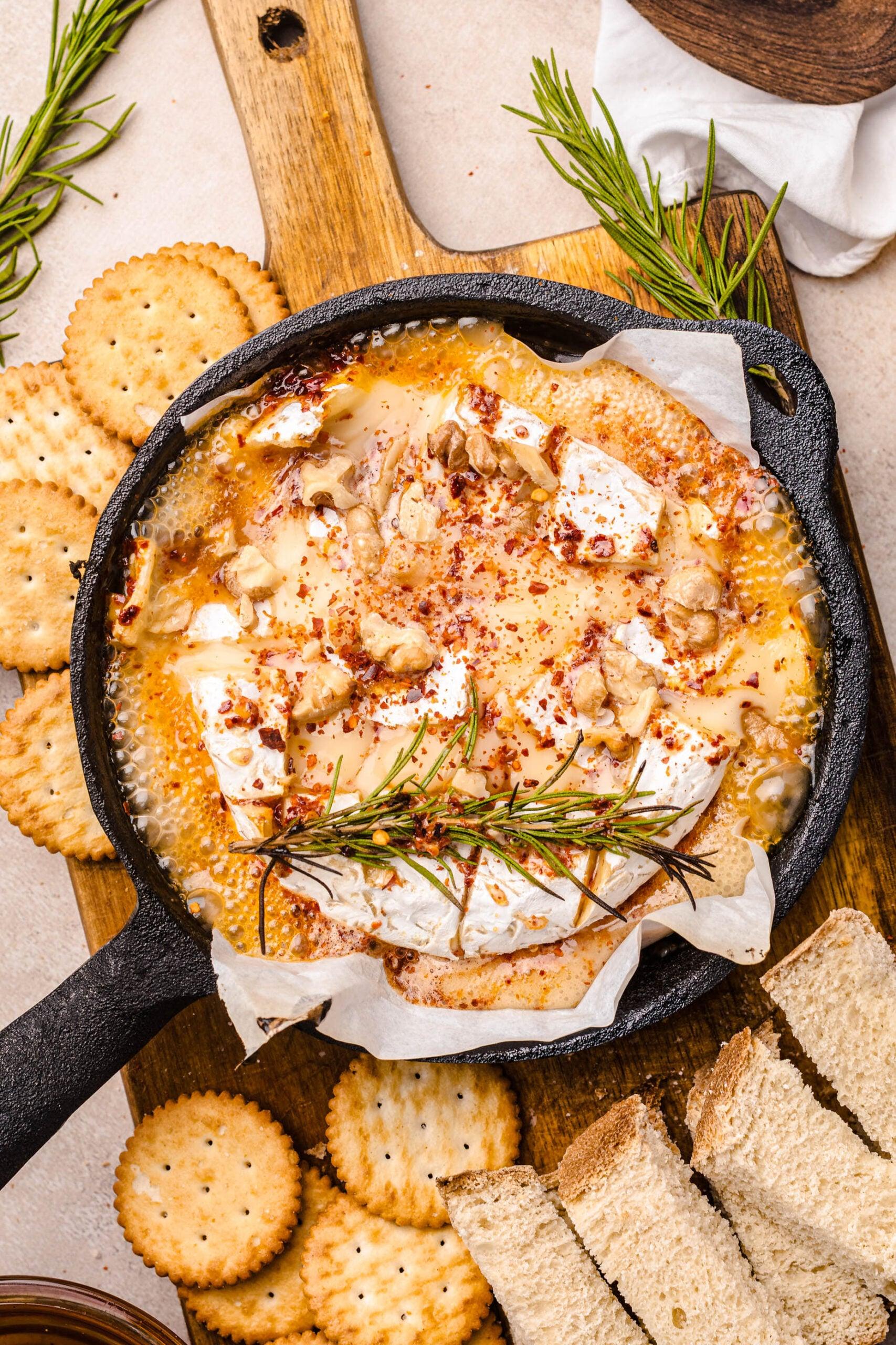 Overhead shot of a hand reaching for a cracker on a charcuterie board with baked camembert