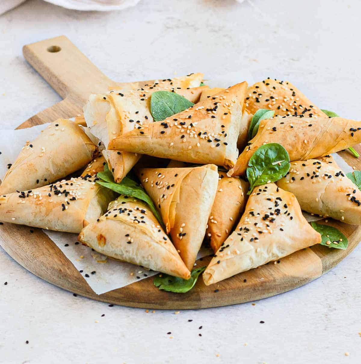 Golden brown spinach feta pastry triangles arranged beautifully on a rustic wooden board, garnished with fresh herbs