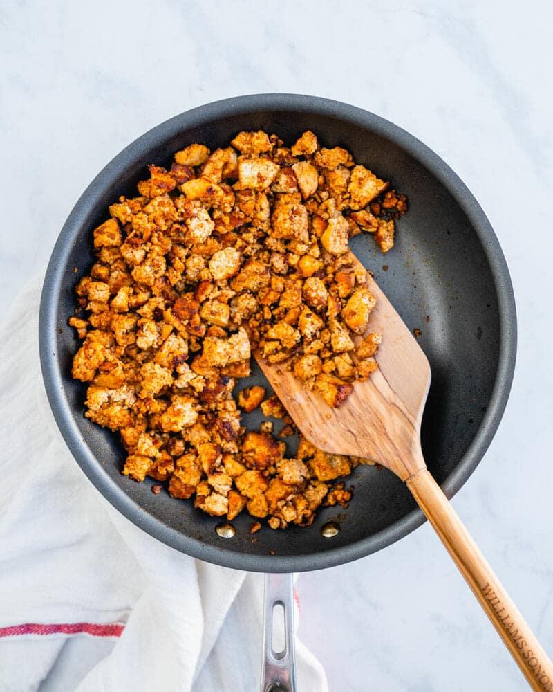 Spices being added to crumbled tofu in a skillet