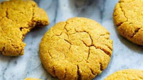 Stack of golden almond cookies on a rustic wooden board, showing crisp edges