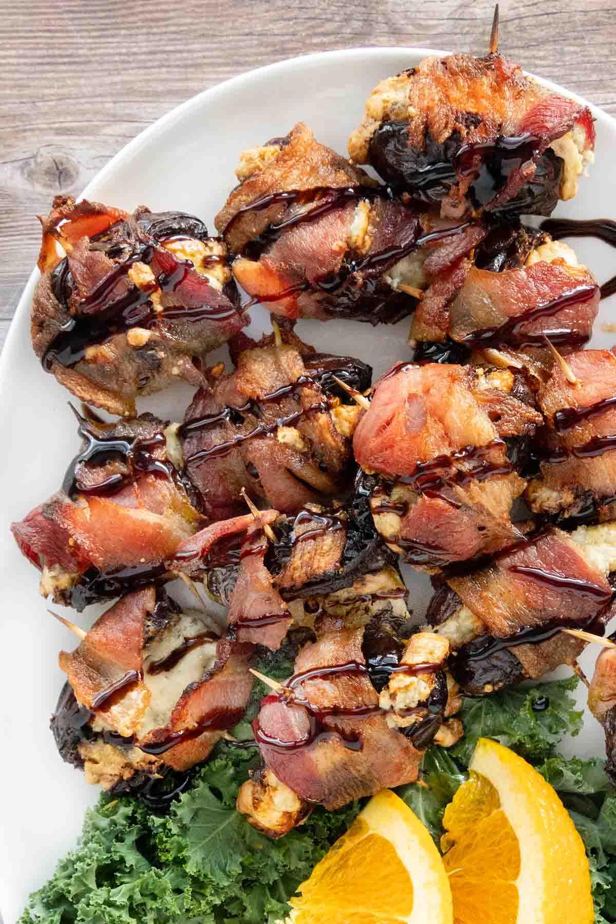 Chef's hands delicately drizzling a glossy balsamic glaze over a platter of freshly baked, sticky bacon-wrapped dates, highlighting their caramelized sheen.