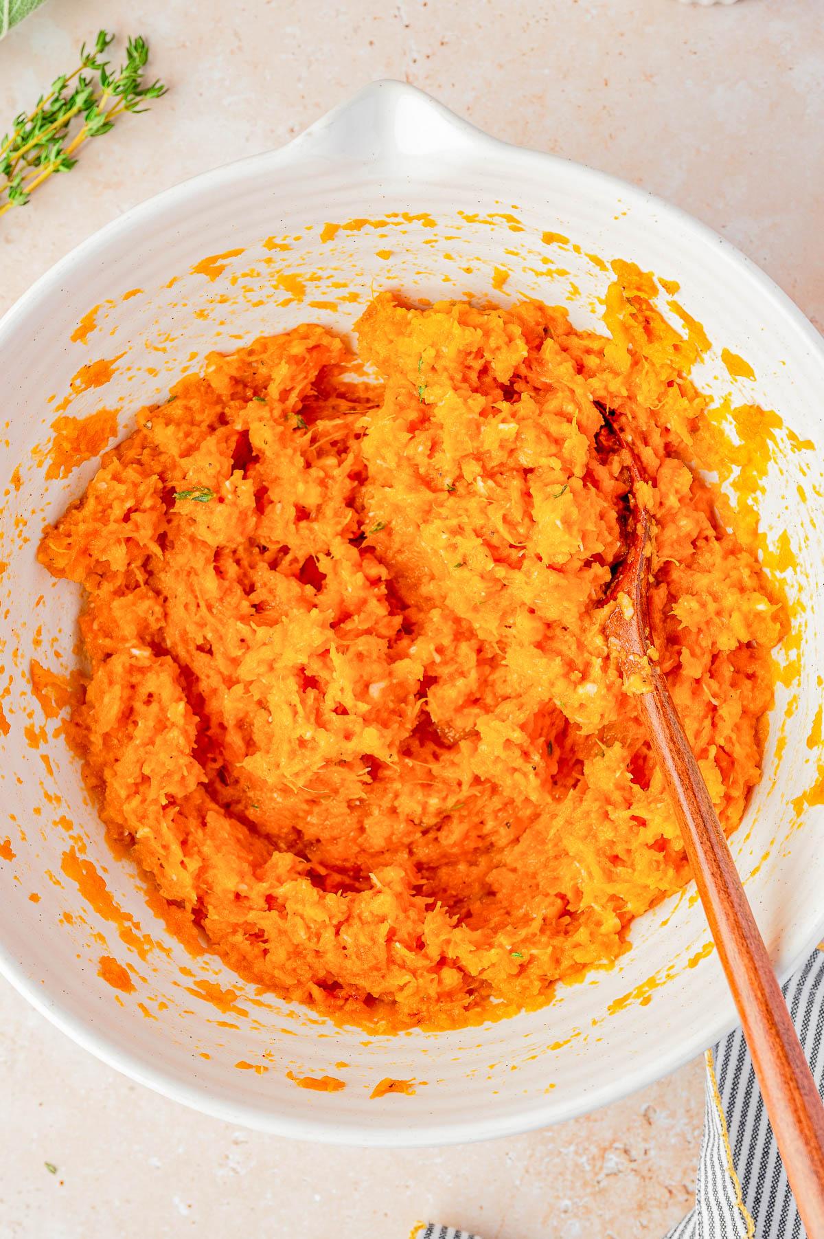 A rustic wooden spoon taking a scoop out of a baked sweet potato casserole