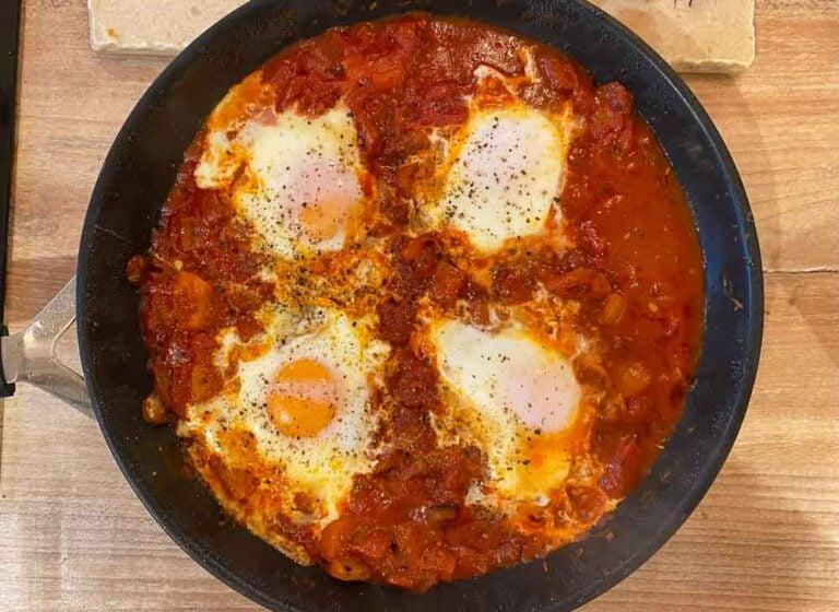 Close-up shot of a fork piercing a runny egg yolk in the shakshuka, revealing the creamy texture