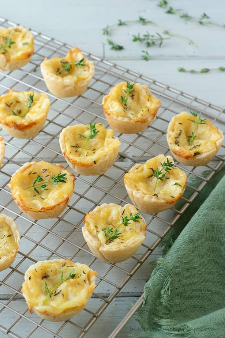Mini cheese tarts with golden savory crust, garnished with herbs on a rustic wooden board