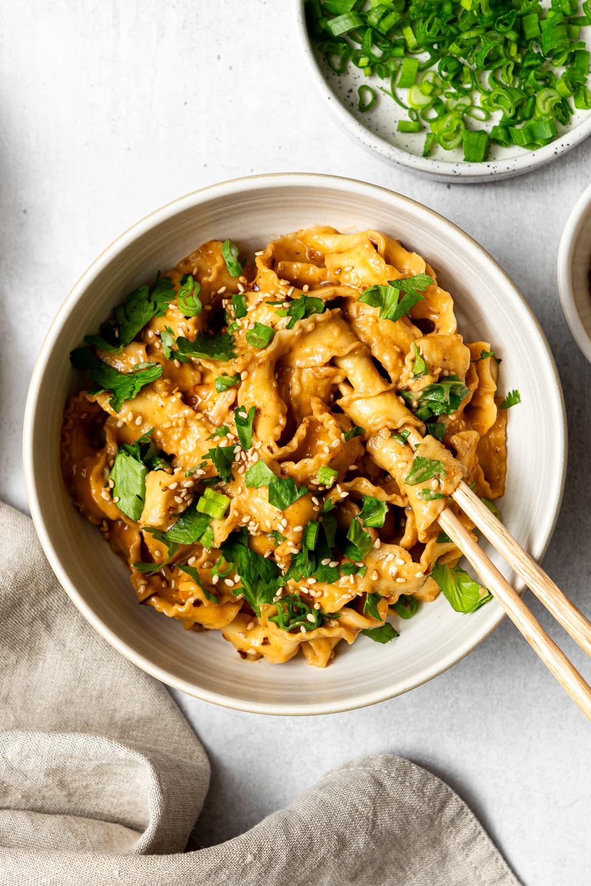 A vibrant bowl of Spicy Sauerkraut and Peanut Noodles, garnished with peanuts and green onions