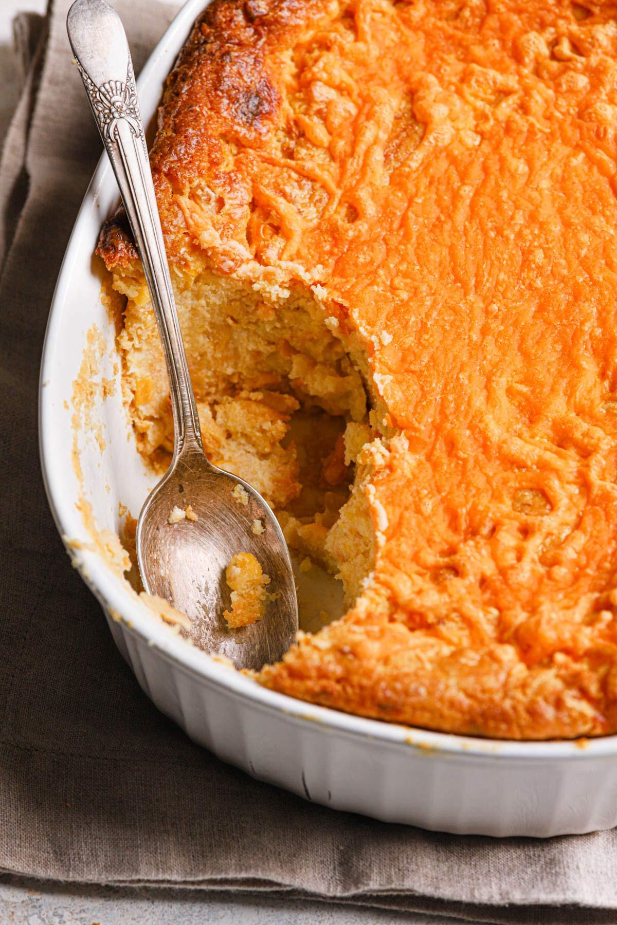 Close-up of golden brown corn casserole with a spoon scooping out a portion, showing creamy texture
