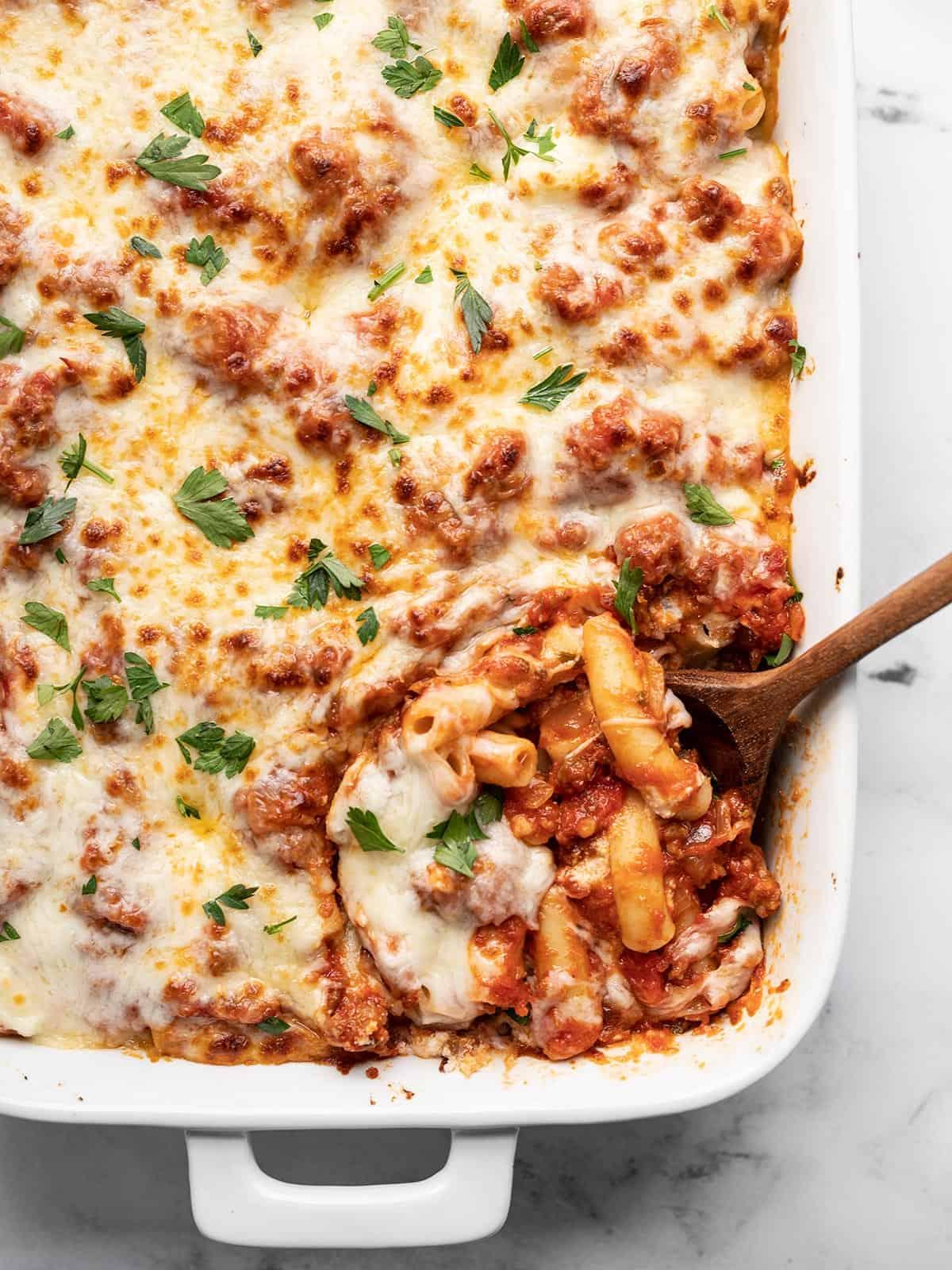 Close-up of baked ziti with a spoon scooping out a serving, showing melted cheese and pasta