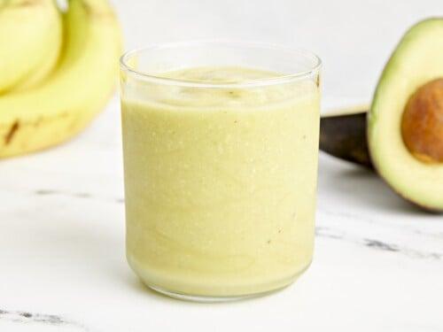 close up shot of a glass filled with avocado smoothie with a spoon inside