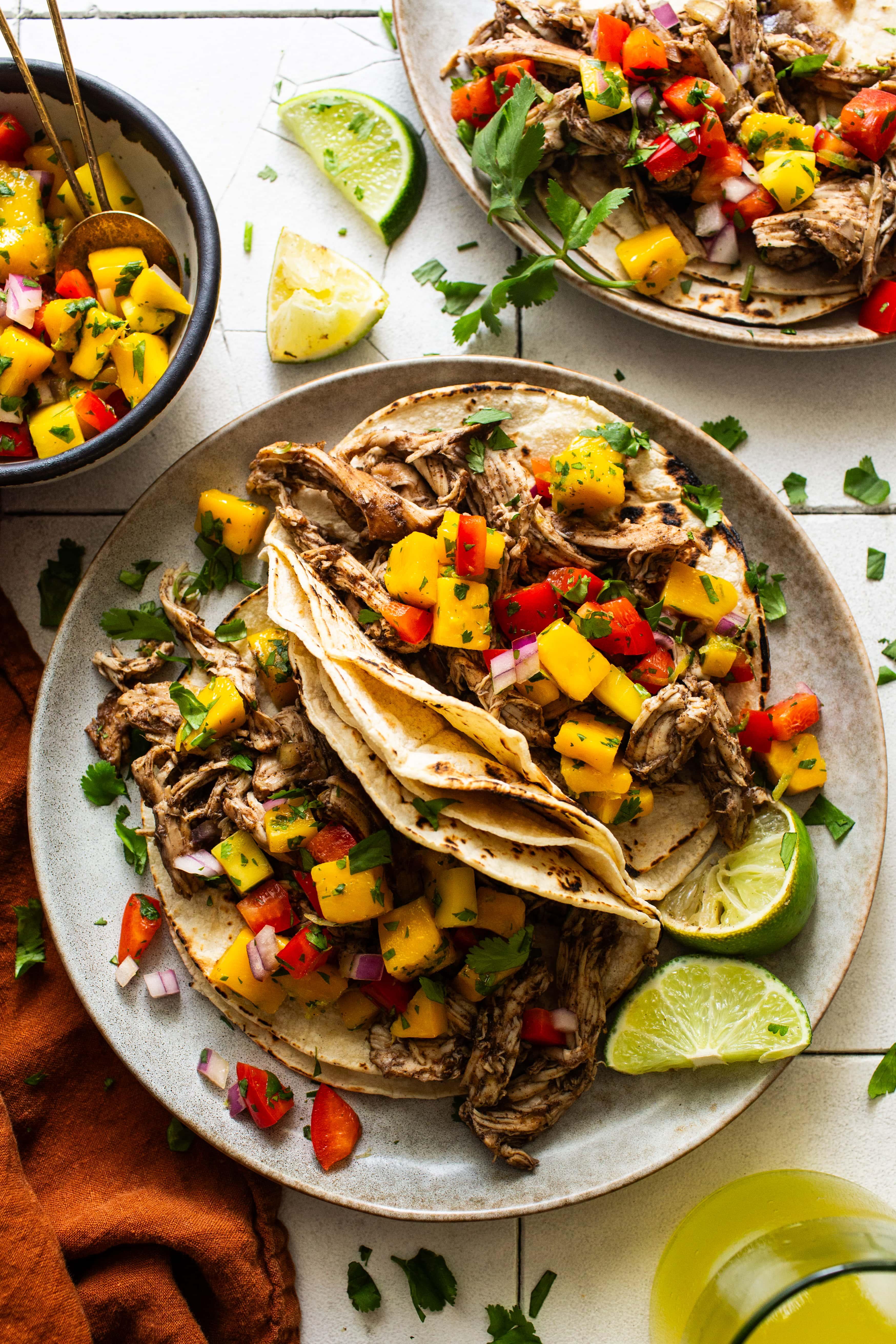 Close-up shot of slow cooker chicken tacos with mango salsa, garnished with cilantro and lime