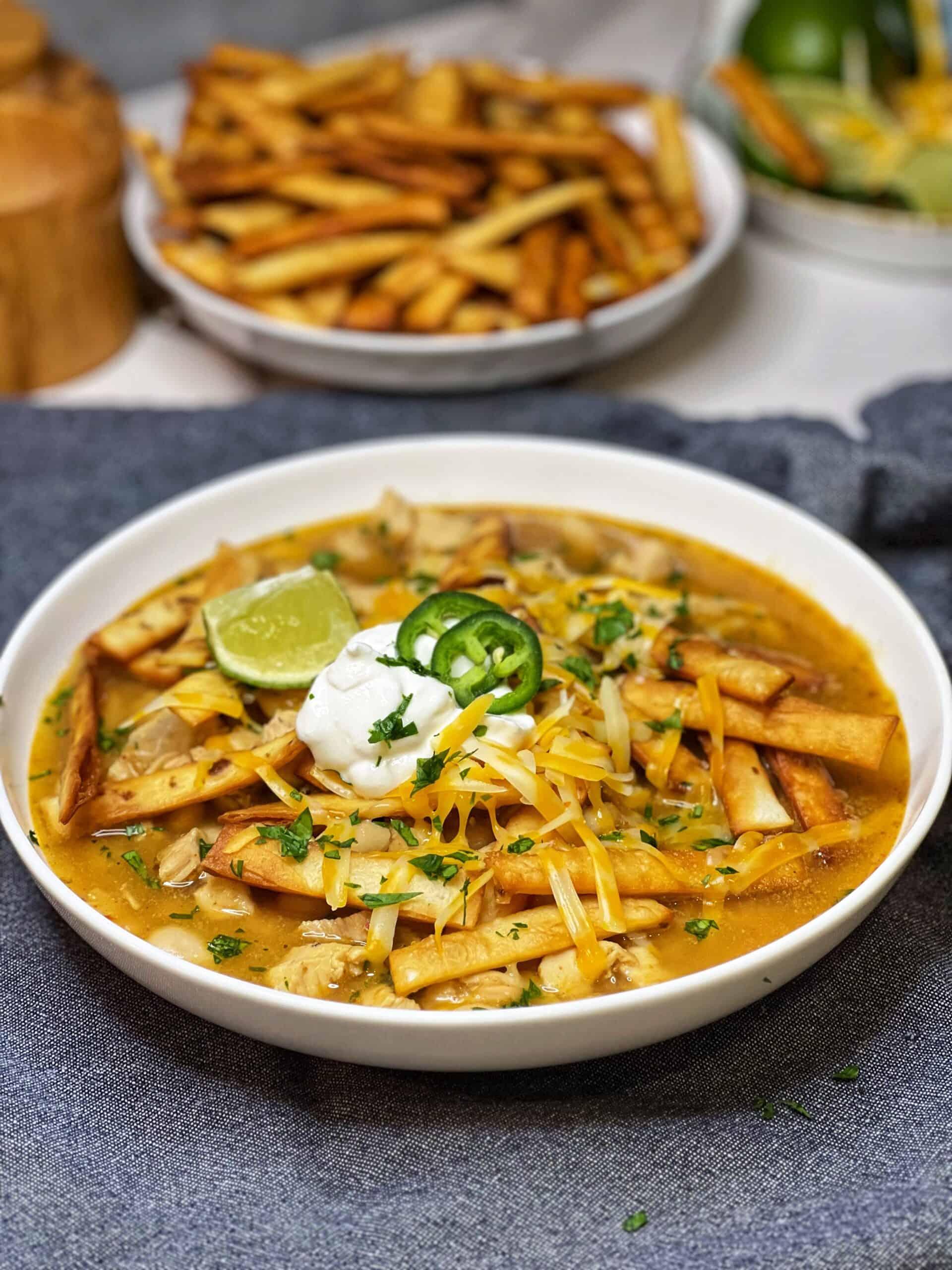 White chicken chili in a cream-colored pot, garnished with fresh cilantro and a dollop of sour cream, cozy kitchen setting