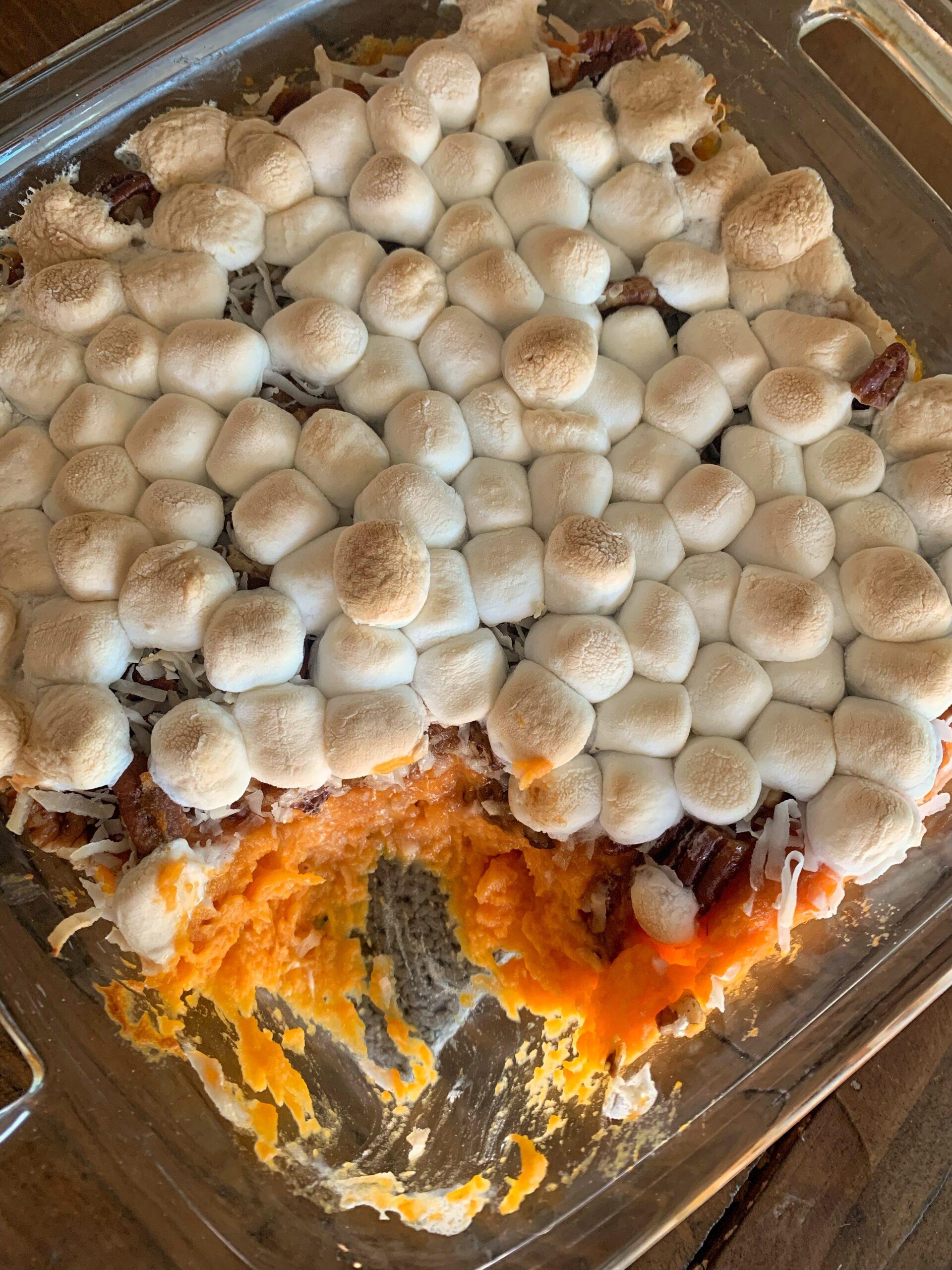 Hands sprinkling toasted coconut over a sweet potato casserole before baking