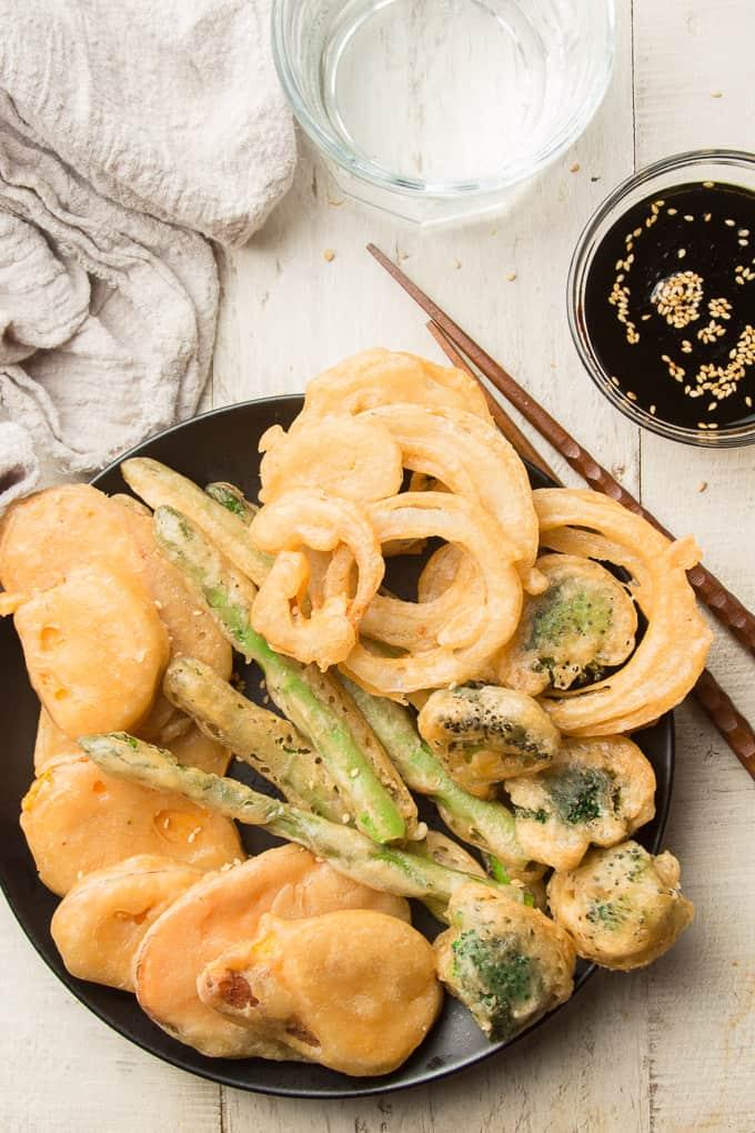 a plate of tempura vegetables with dipping sauce and chopsticks