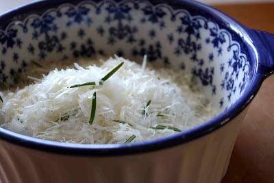 Close-up of a small bowl filled with freshly grated Parmesan cheese and a sprig of rosemary