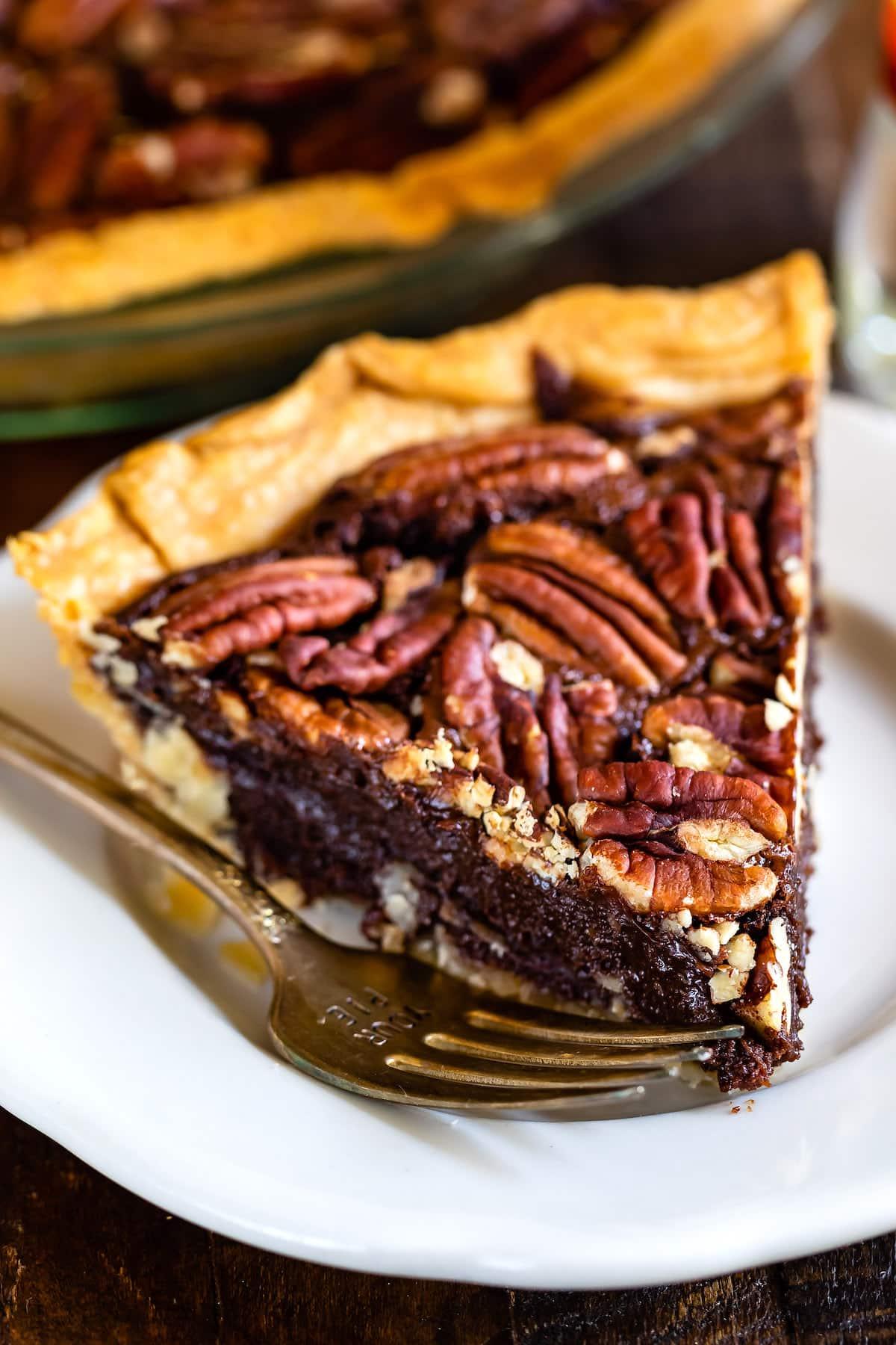 slice of fudgy chocolate pecan pie on a white plate with a fork, cozy kitchen background