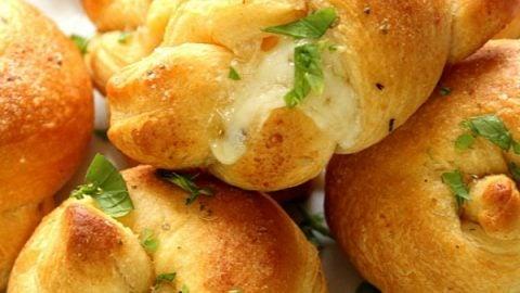 Golden brown garlic knots stuffed with melted cheese on a rustic wooden board, garnished with fresh parsley, perfect for a holiday party.