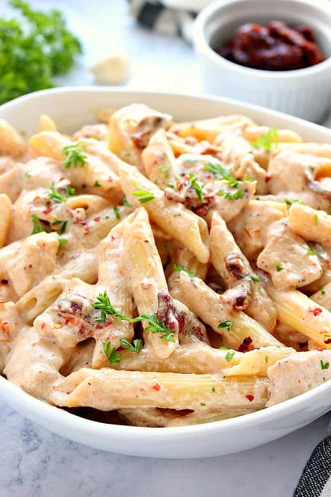Close up shot of a bowl of Chicken Alfredo with sun-dried tomatoes, garnished with parsley