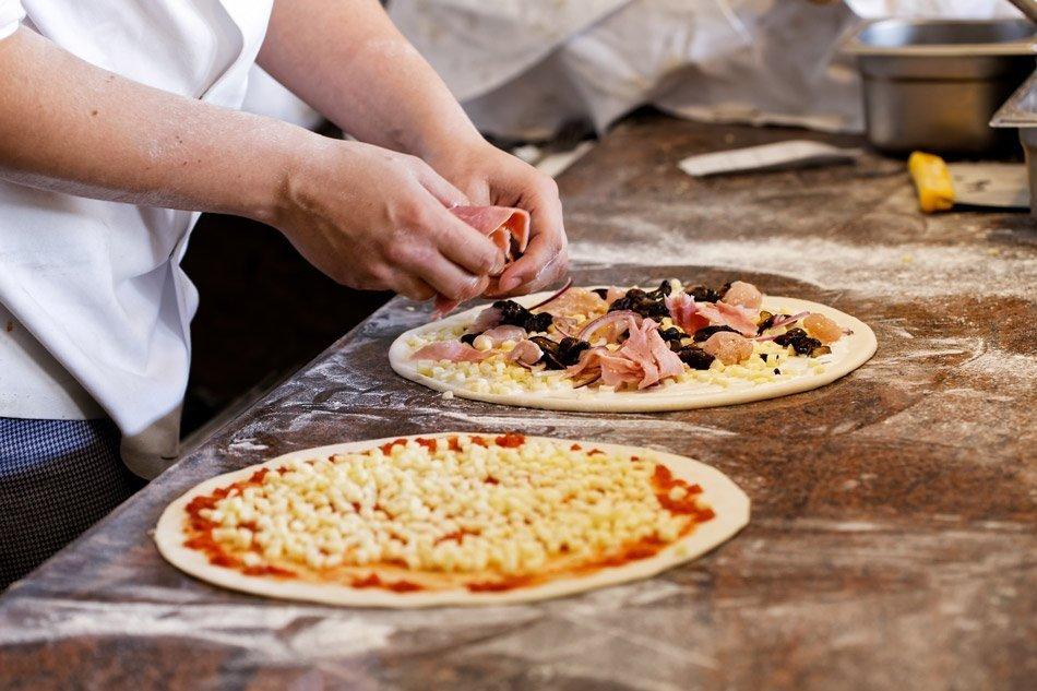 hands carefully placing toppings on a pizza dough