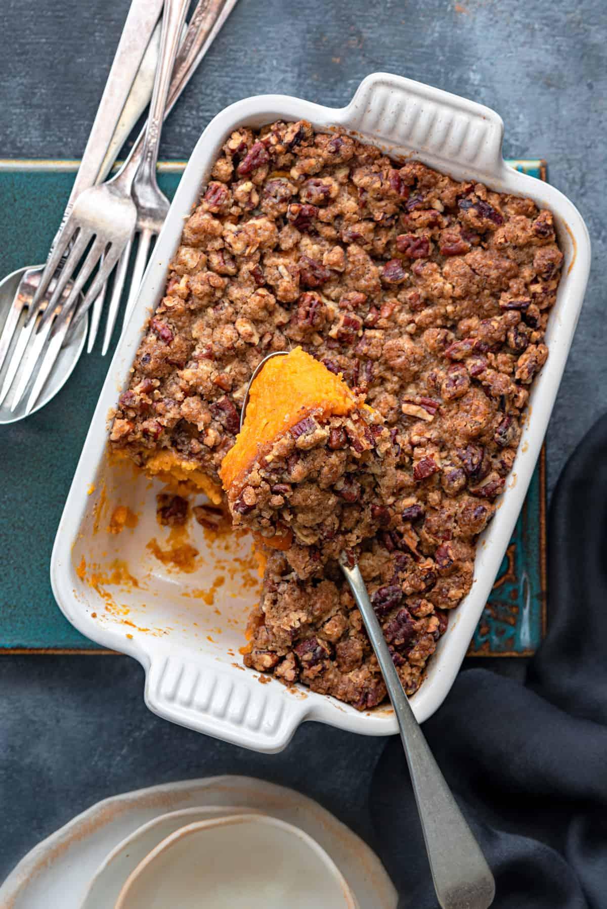 overhead shot of a golden-brown sweet potato casserole with a spoon taking a scoop
